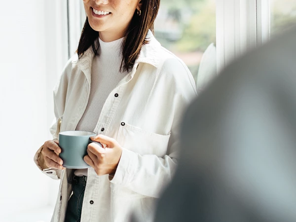 Lächelnde Frau mit Kaffeetasse vor hellem Fenster