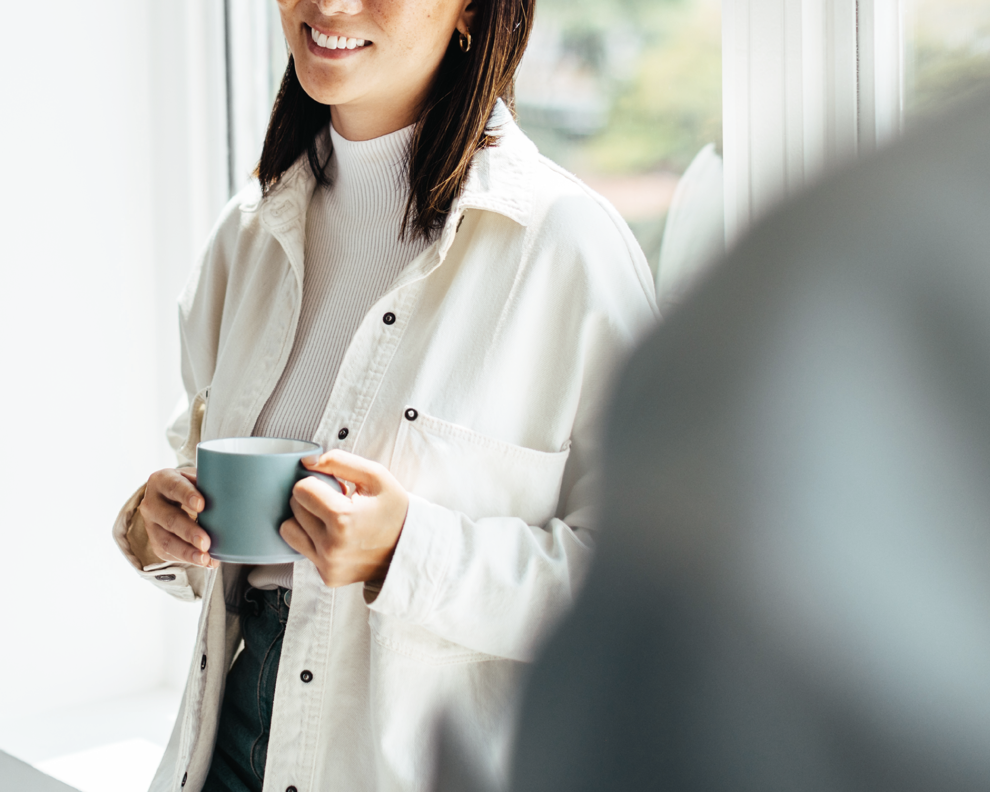 Lächelnde Frau mit Kaffeetasse vor hellem Fenster